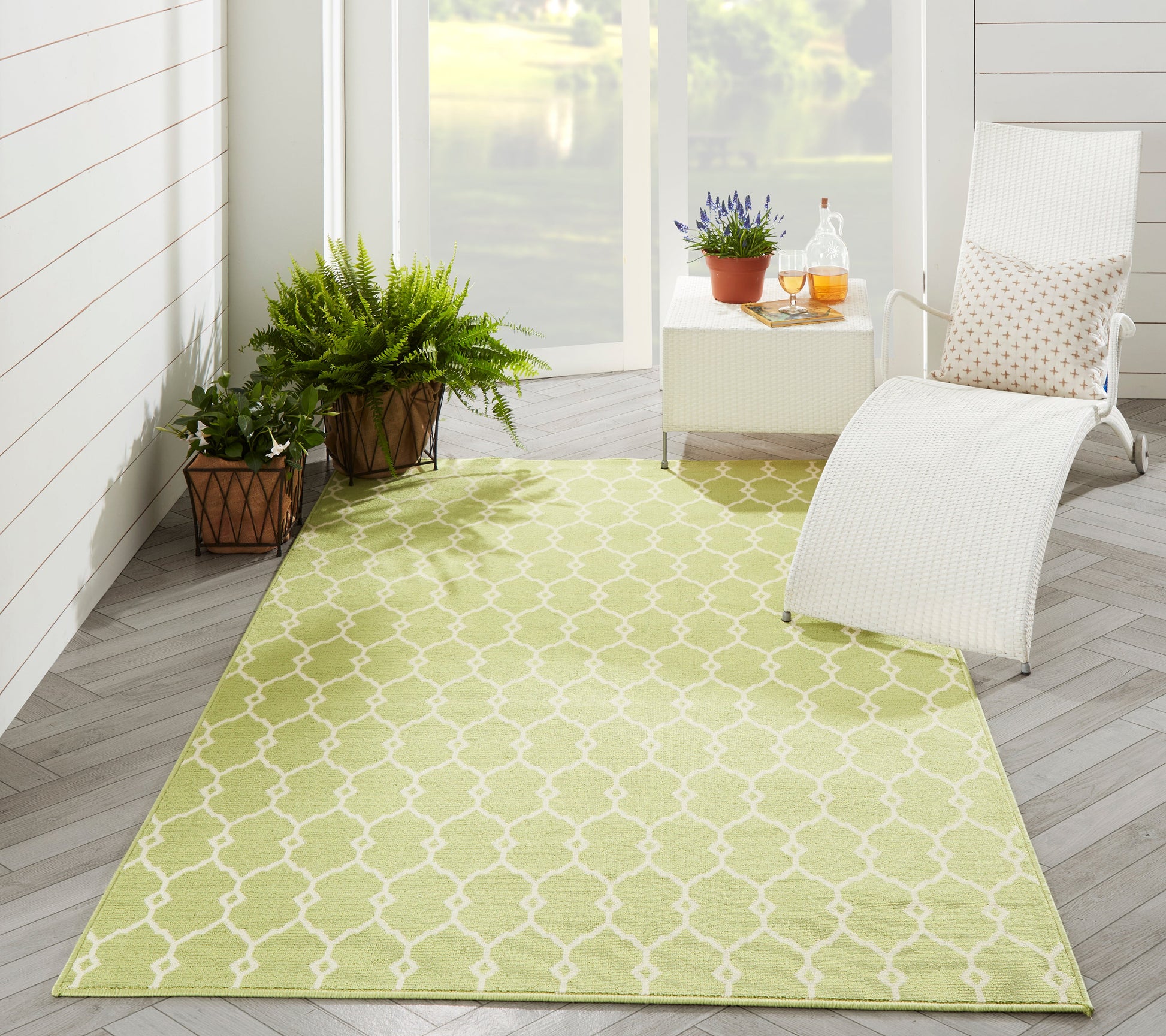 Bright lime green outdoor rug with a white trellis pattern, paired with a white chaise, side table, and potted plants.