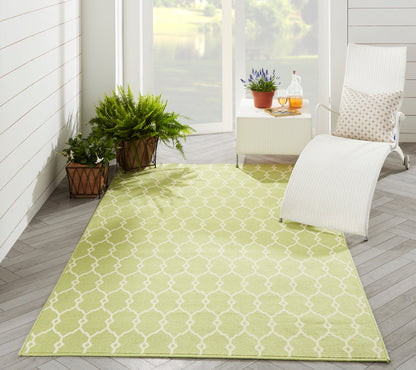 Lime-green trellis outdoor rug on light wood floor, with white lounge chair, side table, and potted plants.
