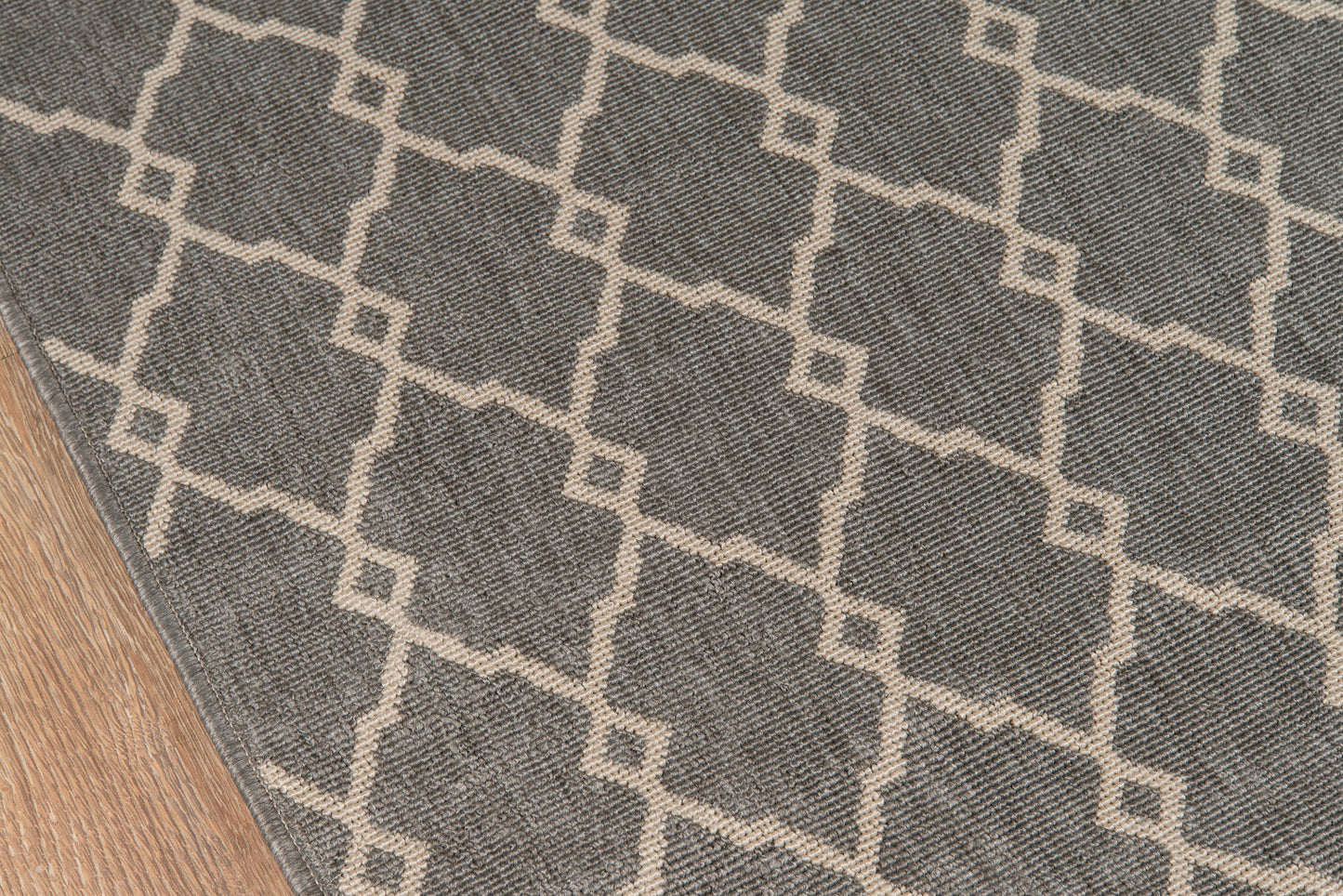 Gray area rug with ivory geometric lattice pattern on wood floor.