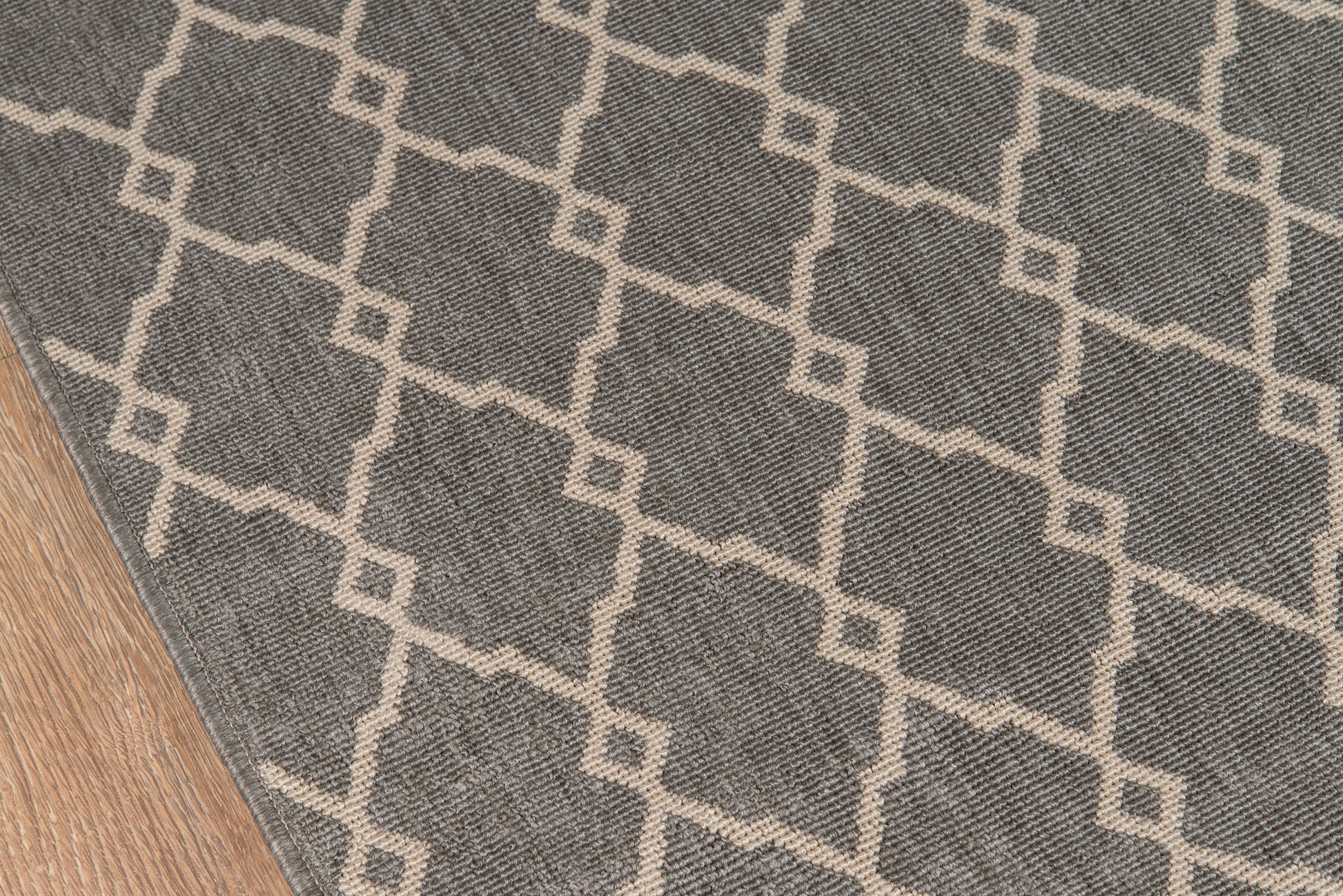 Gray area rug with ivory geometric lattice pattern on wood floor.