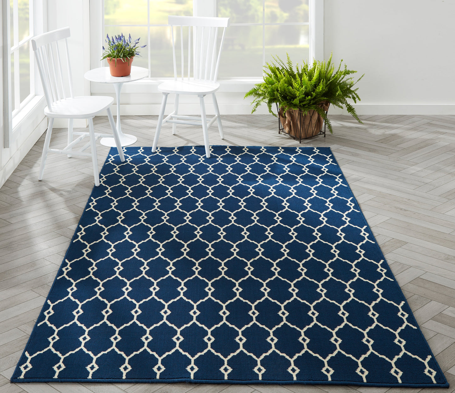 Navy blue rectangular area rug with white lattice pattern in a bright room with white chairs and plants