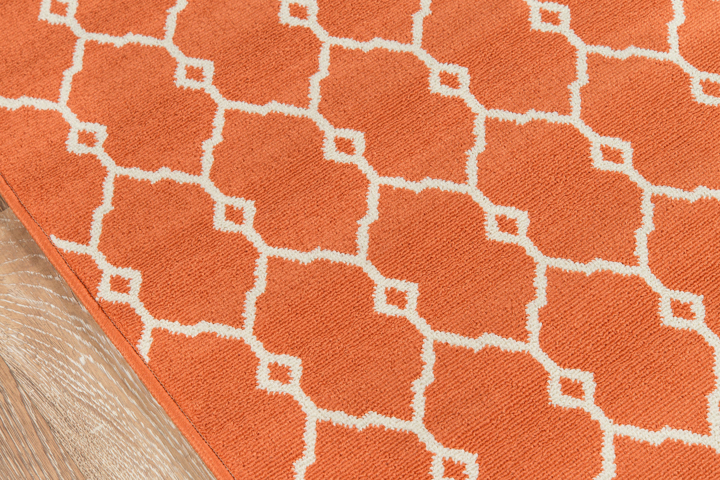 Orange rug with white geometric lattice pattern; corner on wooden floor.