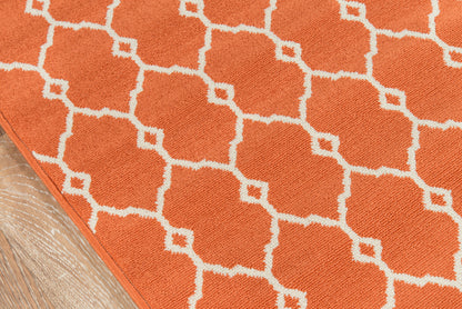 Orange rug with white geometric lattice pattern; corner on wooden floor.