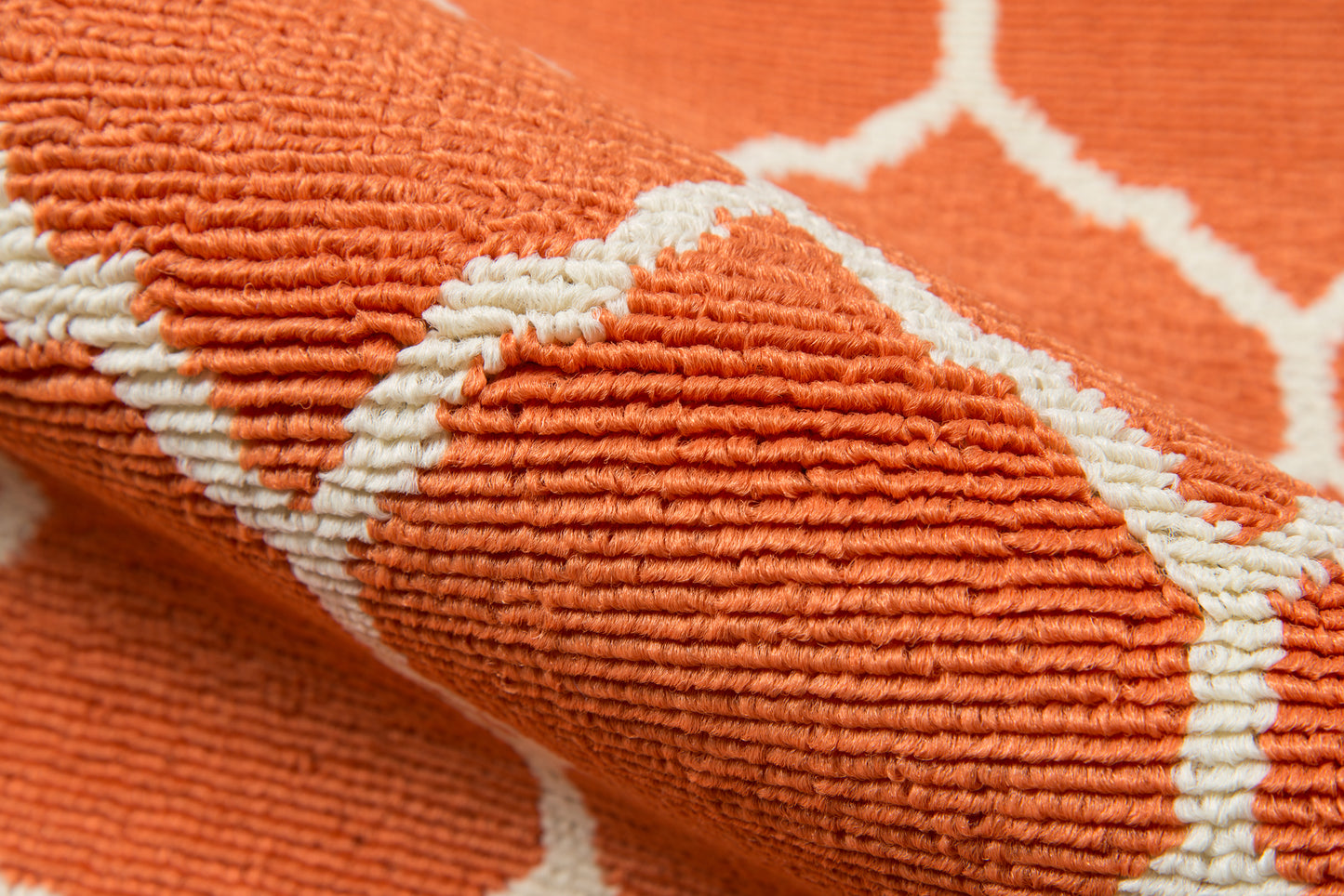 Close-up of an orange tufted rug with white geometric lattice pattern, cozy home decor.