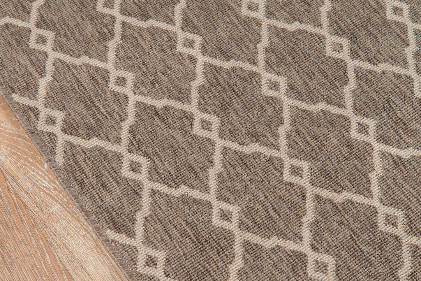 Taupe rug with cream geometric lattice pattern and woven texture on light wood floor.