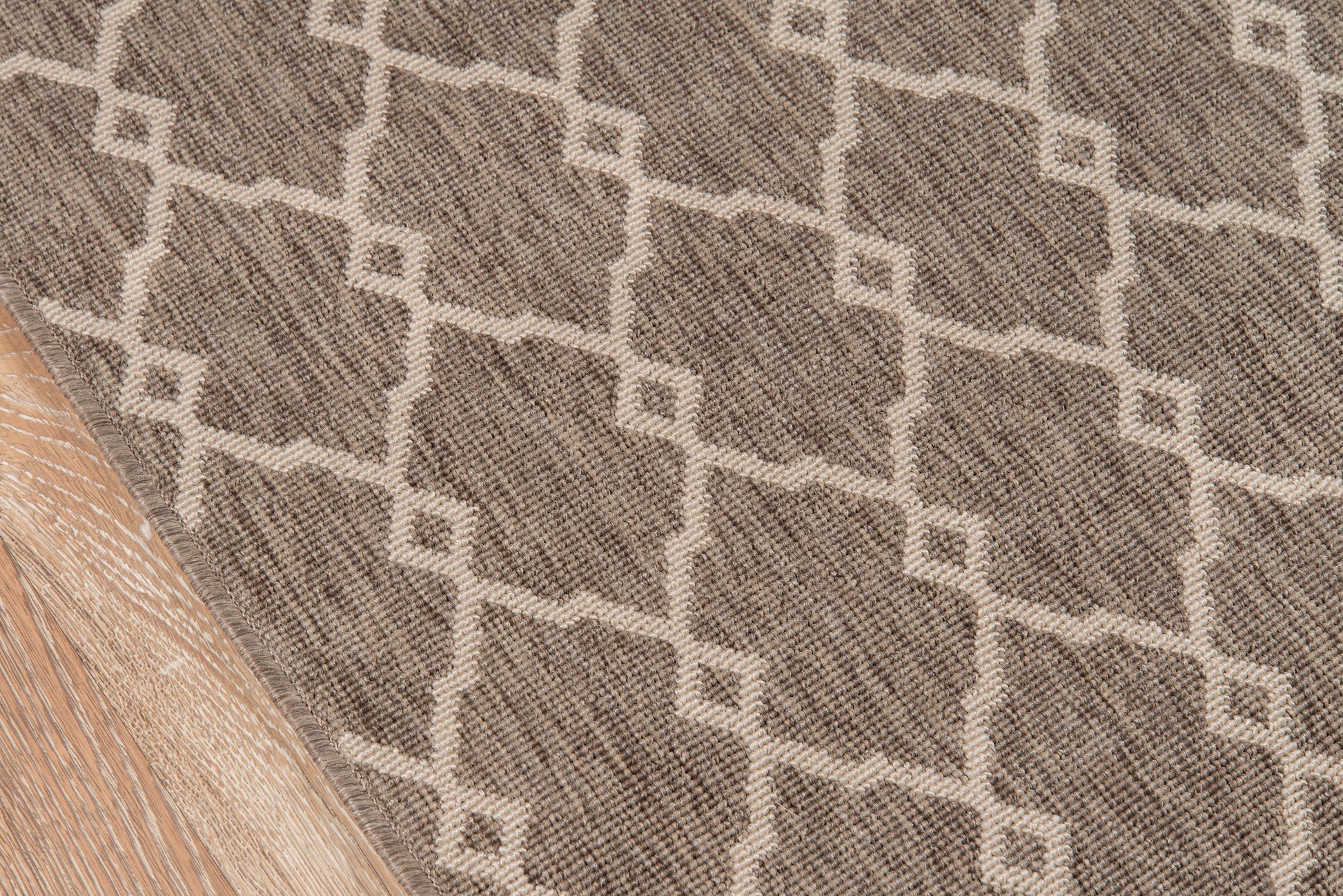 Taupe rug with cream geometric lattice pattern and woven texture on light wood floor.