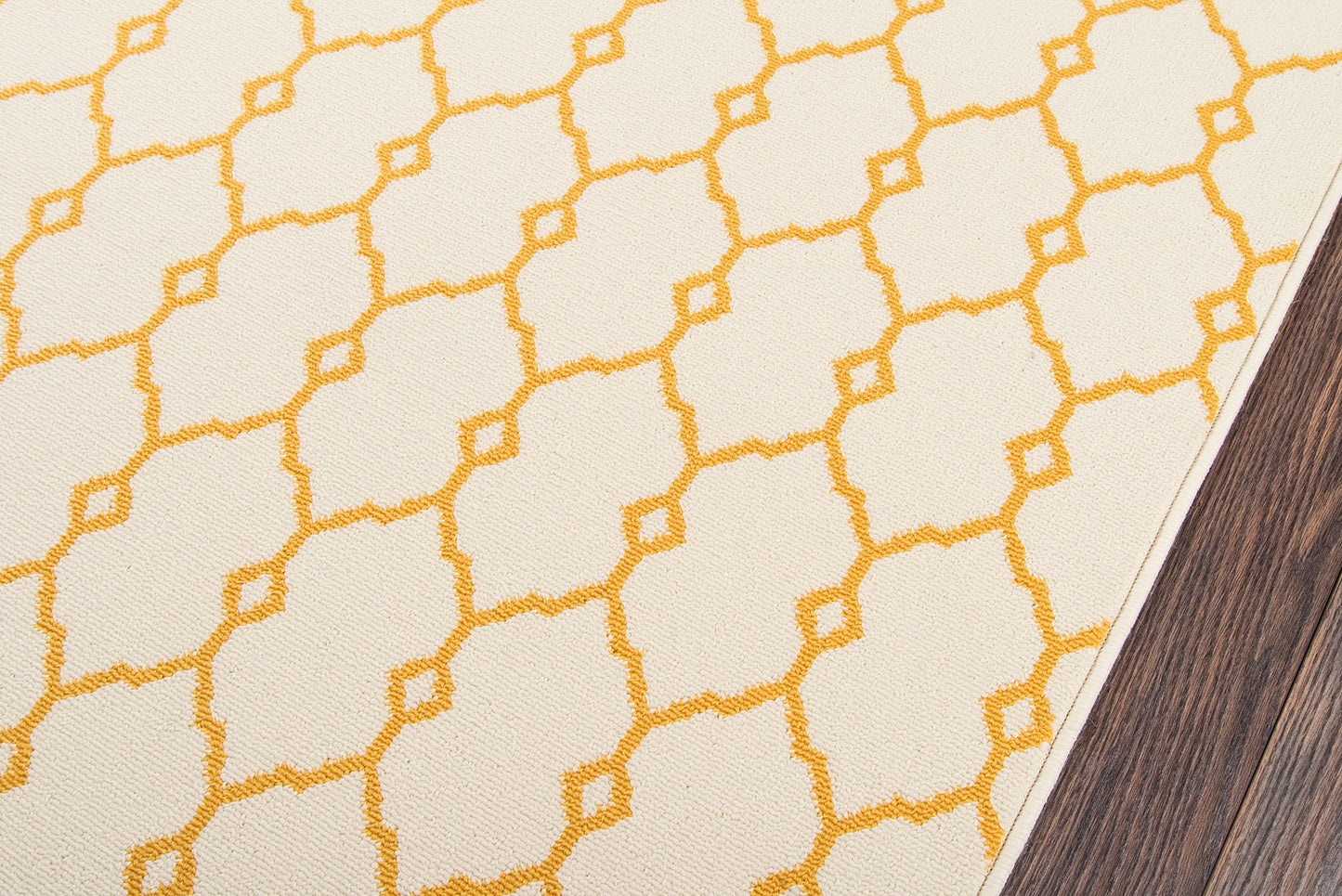 Cream area rug with bright yellow geometric lattice pattern, shown on dark wood flooring.