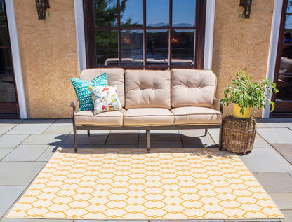 Beige outdoor sofa with metal frame, teal floral cushions, on a yellow honeycomb rug beside a wicker plant basket.