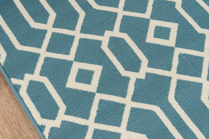 Blue area rug with white geometric interlocking square pattern on wooden floor.