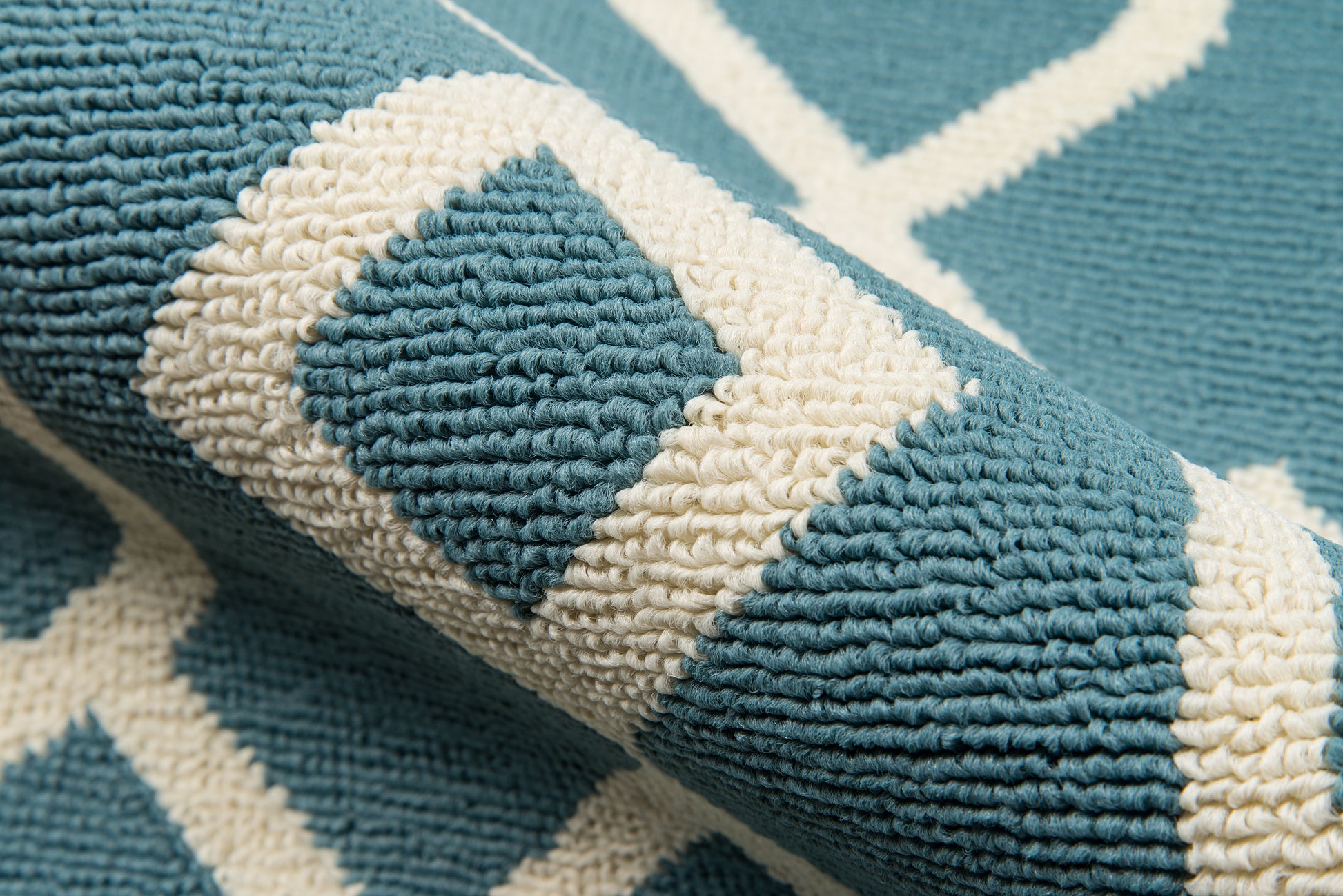 Teal blue rug with white geometric lattice pattern, thick tufted pile, rolled edge.