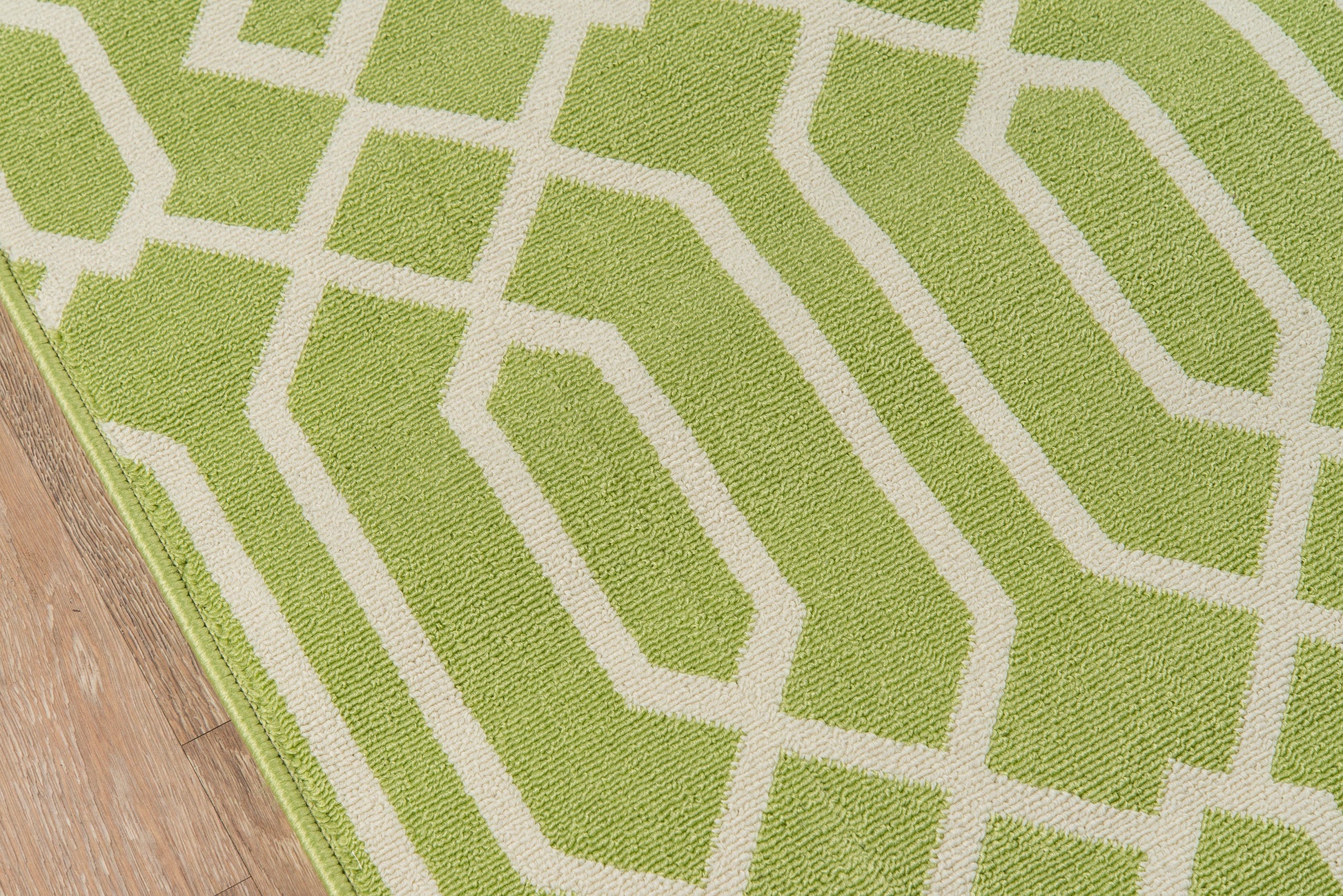 Lime green rug with a white geometric lattice pattern on a wooden floor.
