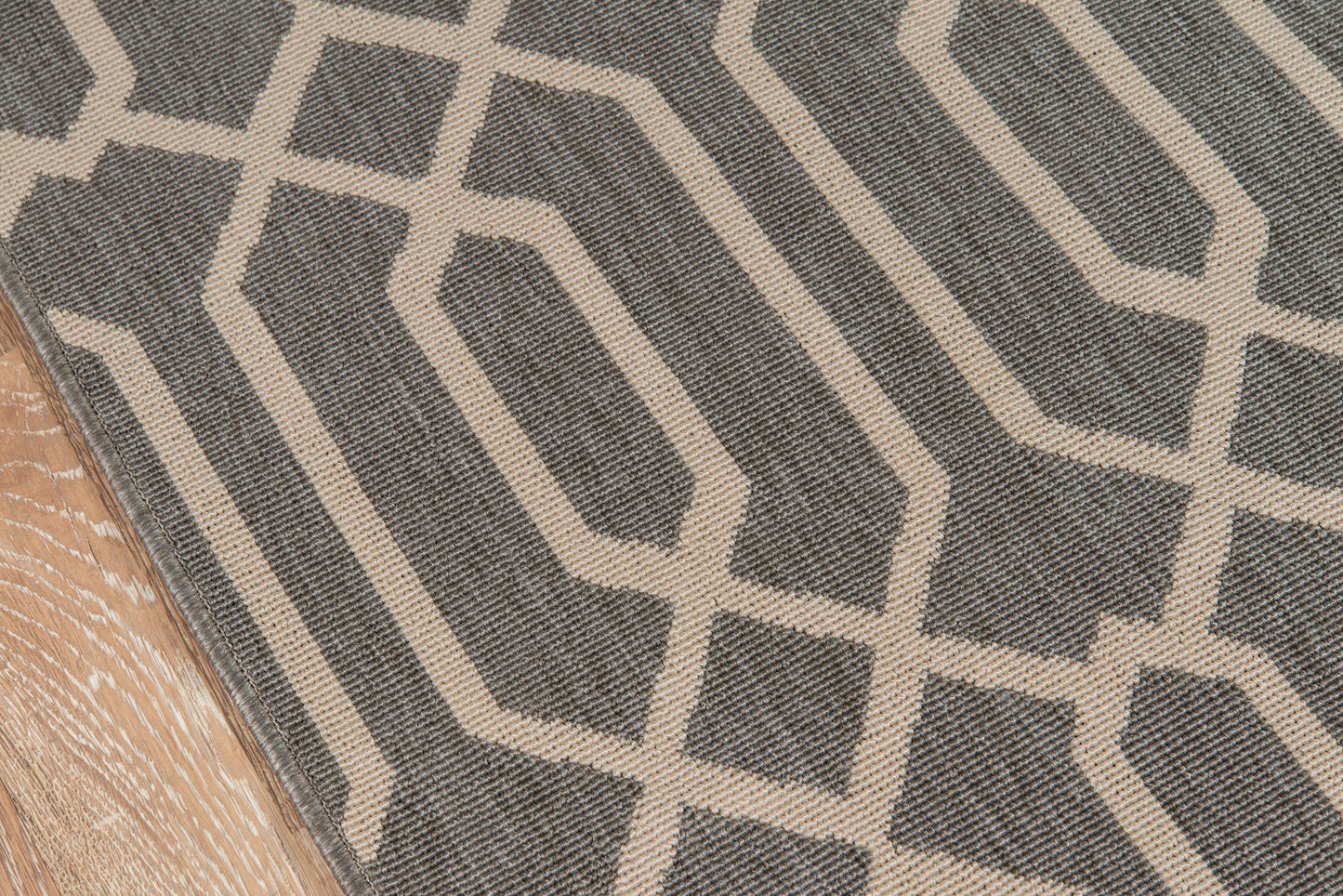 Rectangular gray rug with white geometric interlocking hexagon pattern, edge on light wood floor.