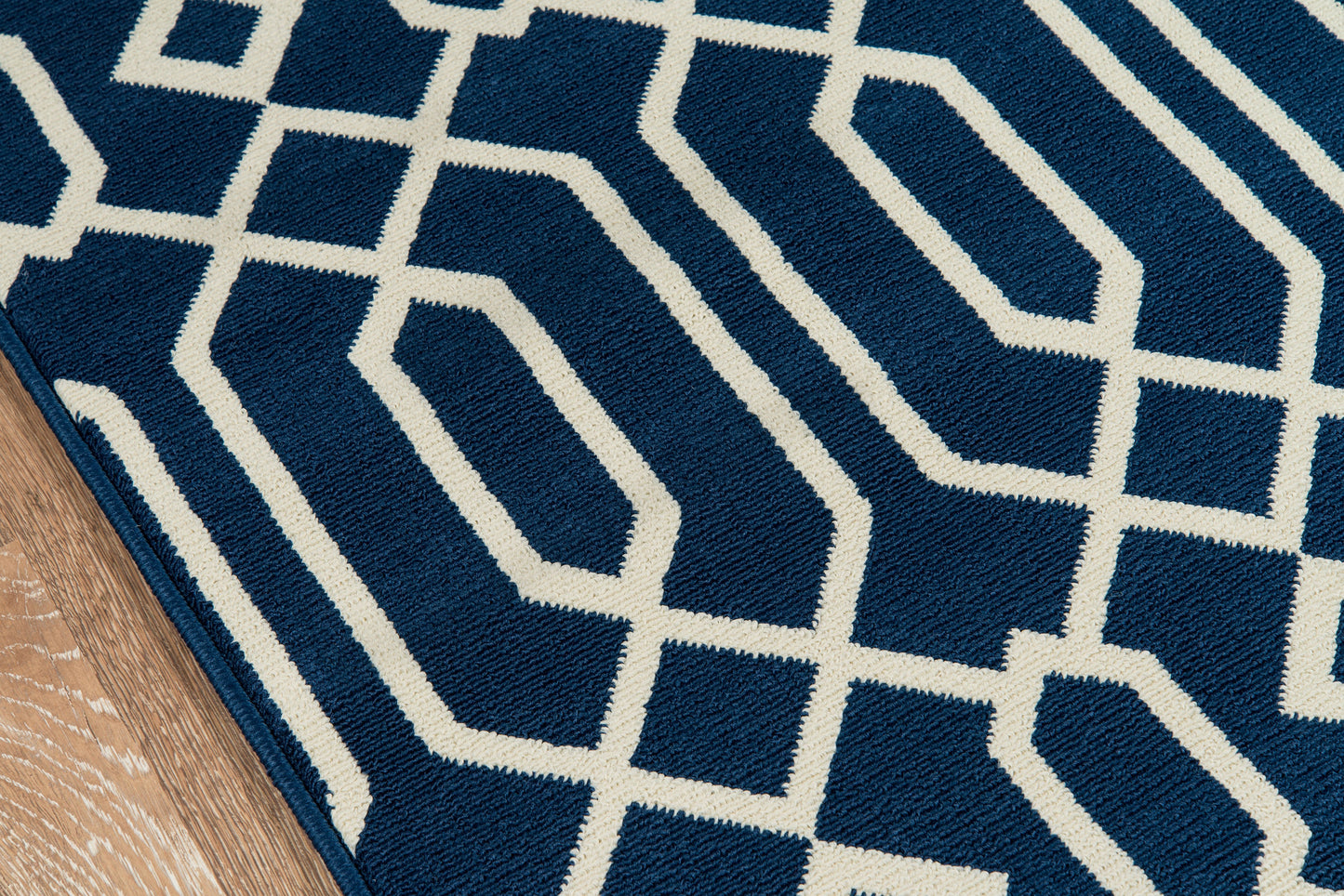 Navy blue rug with white geometric lattice pattern; plush textured pile on hardwood floor.