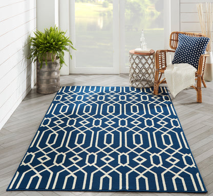 Navy blue area rug with white geometric lattice pattern in a sunlit living room; potted plant and wicker chair nearby.