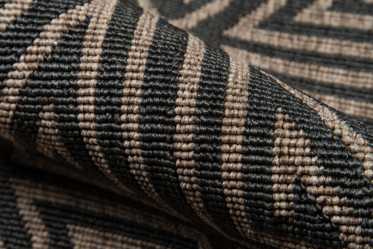 Close-up of a black and beige woven rug with geometric chevron pattern and textured fibers.