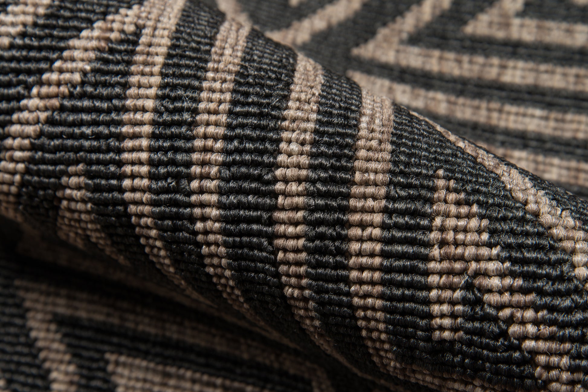 Close-up of a black and beige woven rug with geometric chevron pattern and textured fibers.