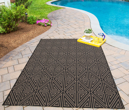Outdoor geometric area rug, 2' x 4', in charcoal black with a tan triangular pattern on a brick poolside patio.
