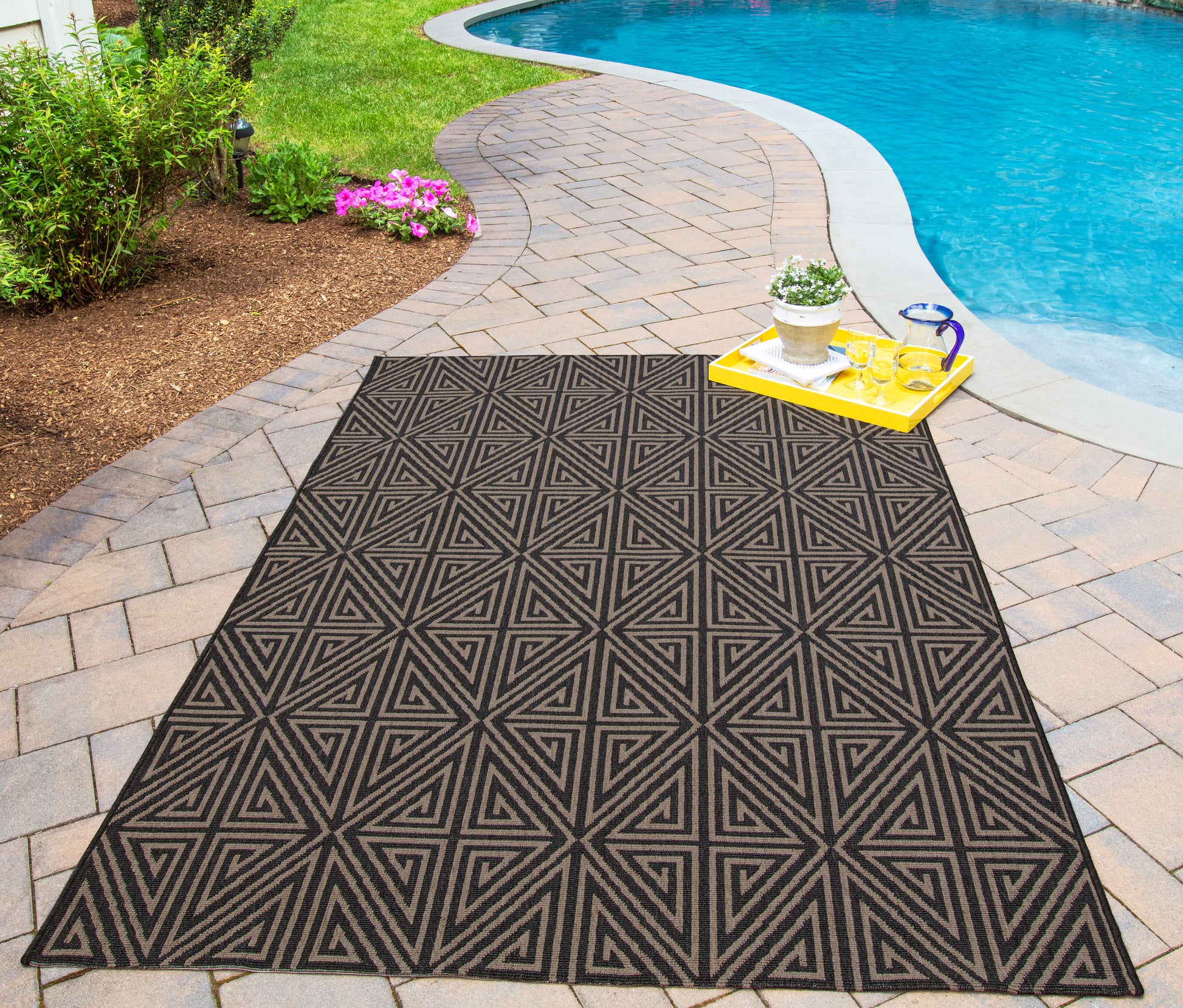 Outdoor geometric rug in black and tan triangles on a curved poolside paver, with a yellow tray nearby.
