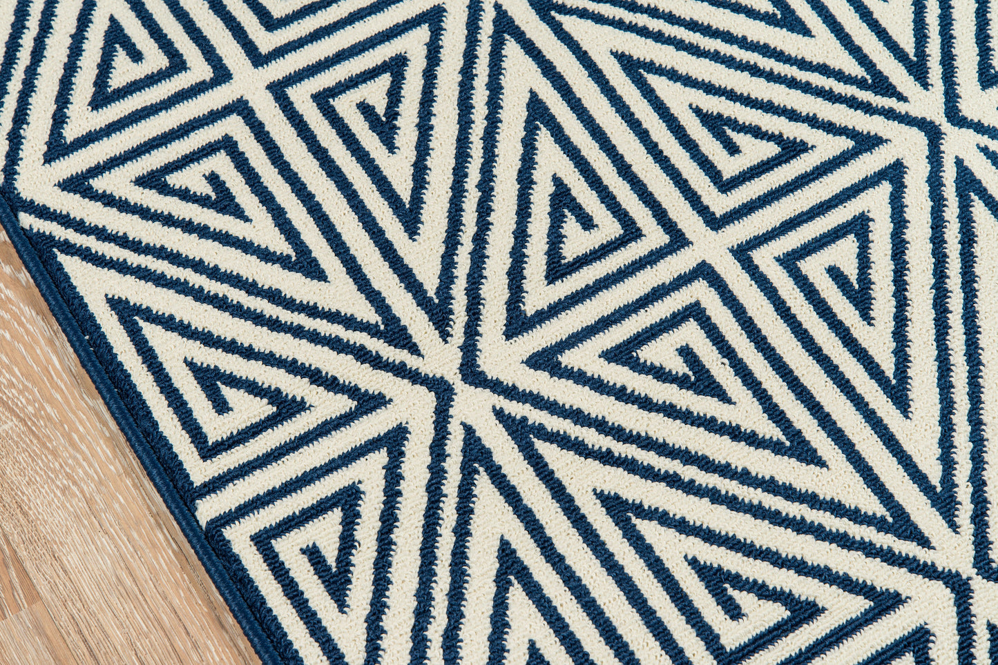 Navy blue geometric rug with white triangular motif on cream background, shown on wood floor.