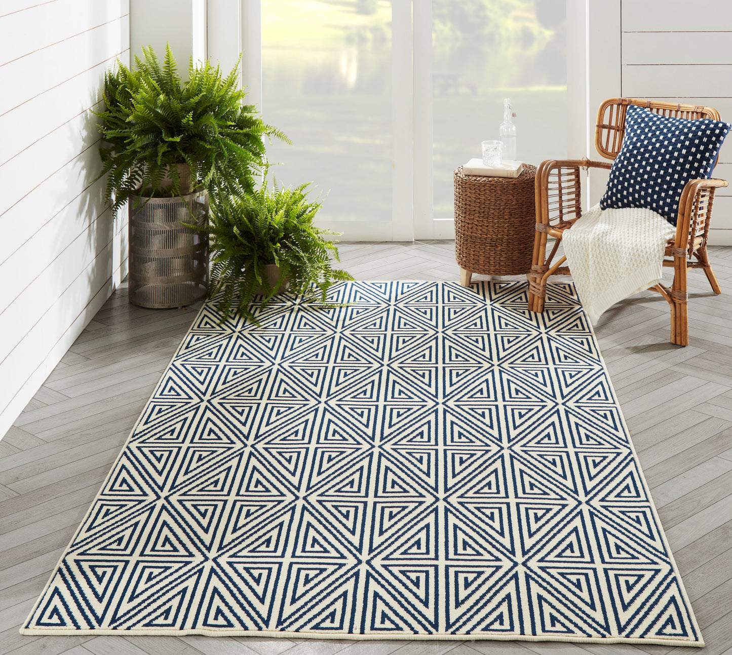 Geometric navy and white star-pattern outdoor rug on a sunlit porch with rattan chairs and lush ferns.