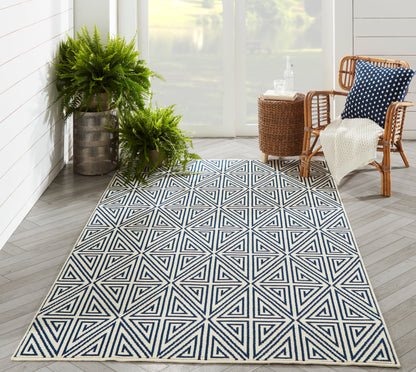 Geometric navy and white star-pattern outdoor rug on a sunlit porch with rattan chairs and lush ferns.