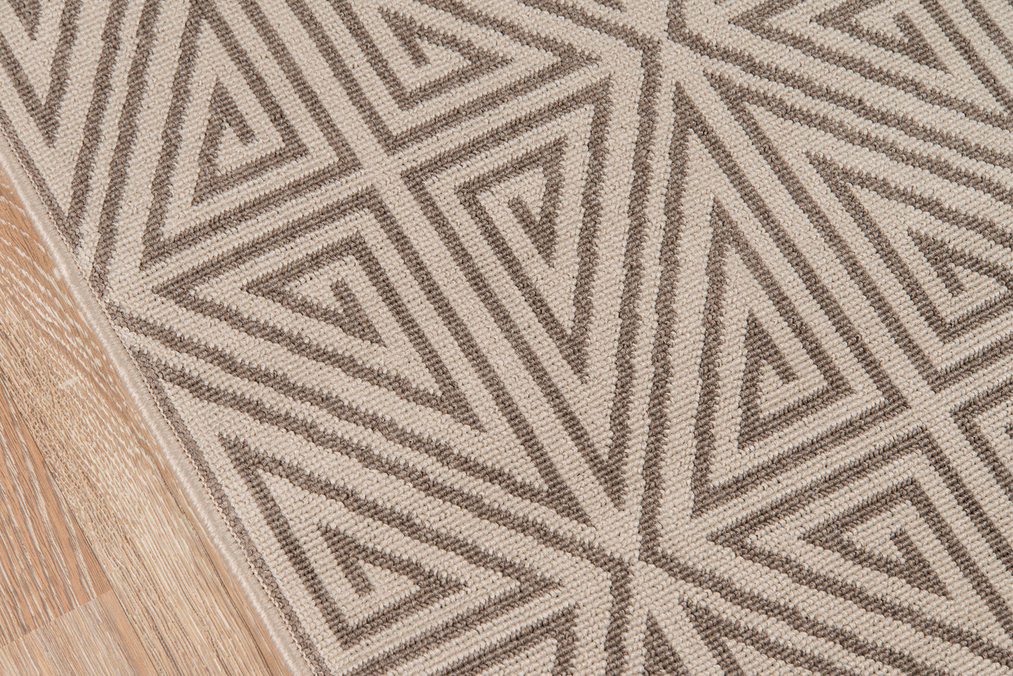 Taupe & beige geometric woven rug with triangular motif on wood floor.