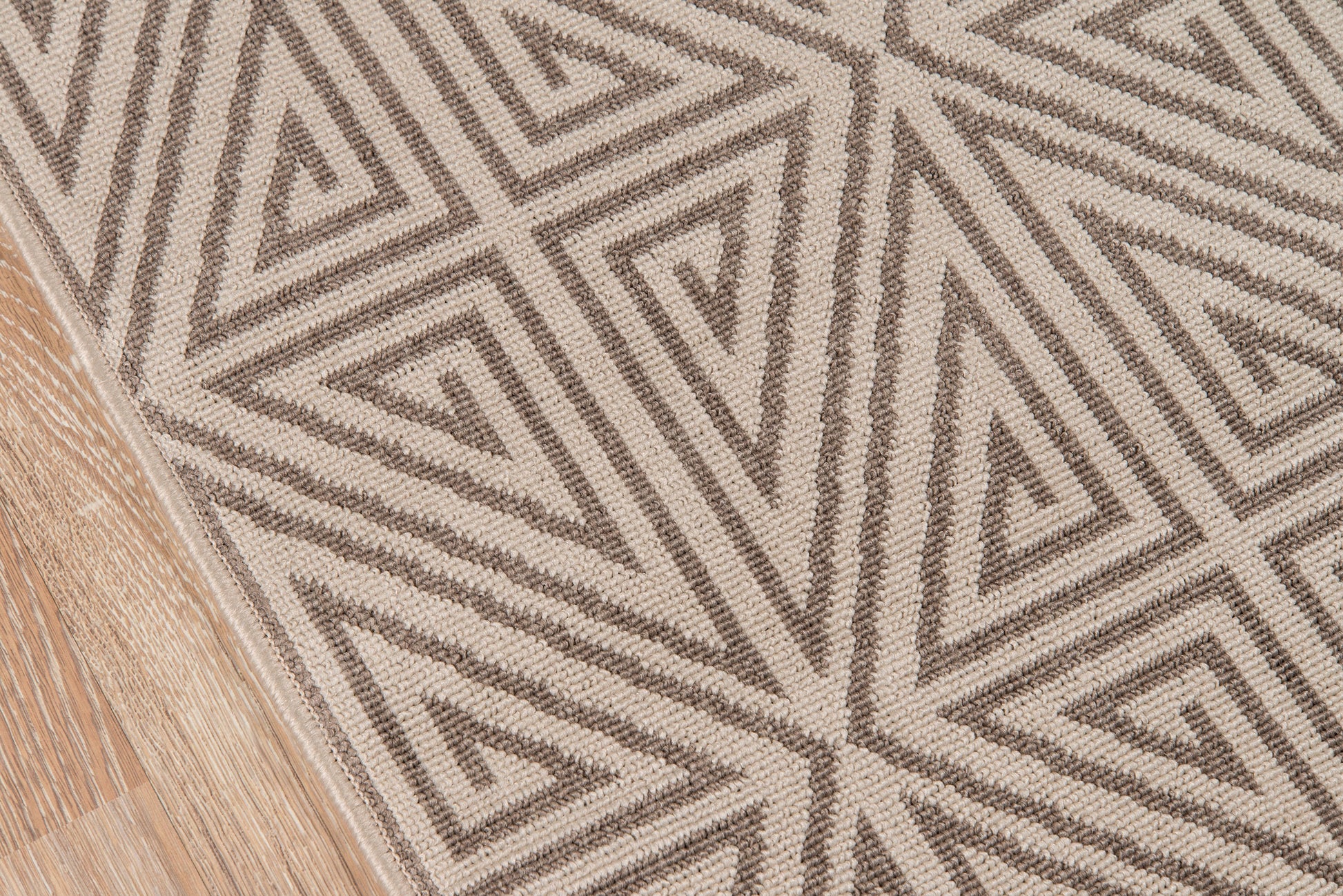 Taupe & beige geometric woven rug with triangular motif on wood floor.