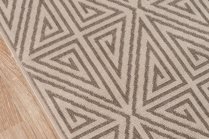 Geometric taupe and beige woven rug with triangular maze pattern on wood floor.