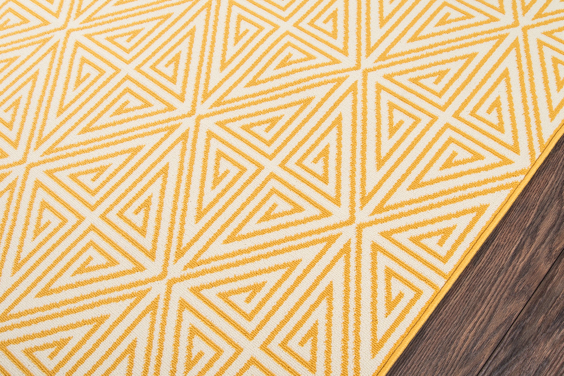 Golden-yellow geometric rug with triangle motif on cream background, yellow border, on dark wood floor.