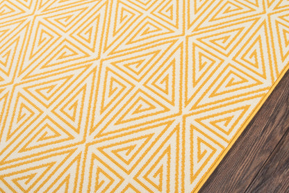 Golden-yellow geometric rug with triangle motif on cream background, yellow border, on dark wood floor.