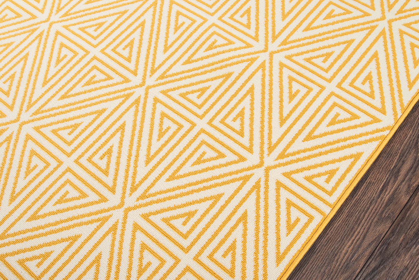 Mustard yellow woven rug with white geometric triangular pattern on dark wood floor.