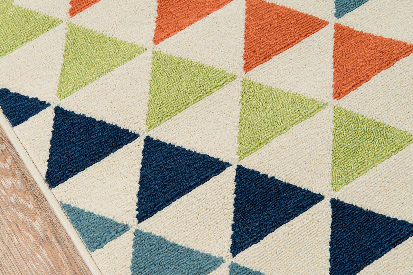 Colorful geometric triangle rug with lime green, orange, navy and teal triangles on cream background, edge on wooden floor.