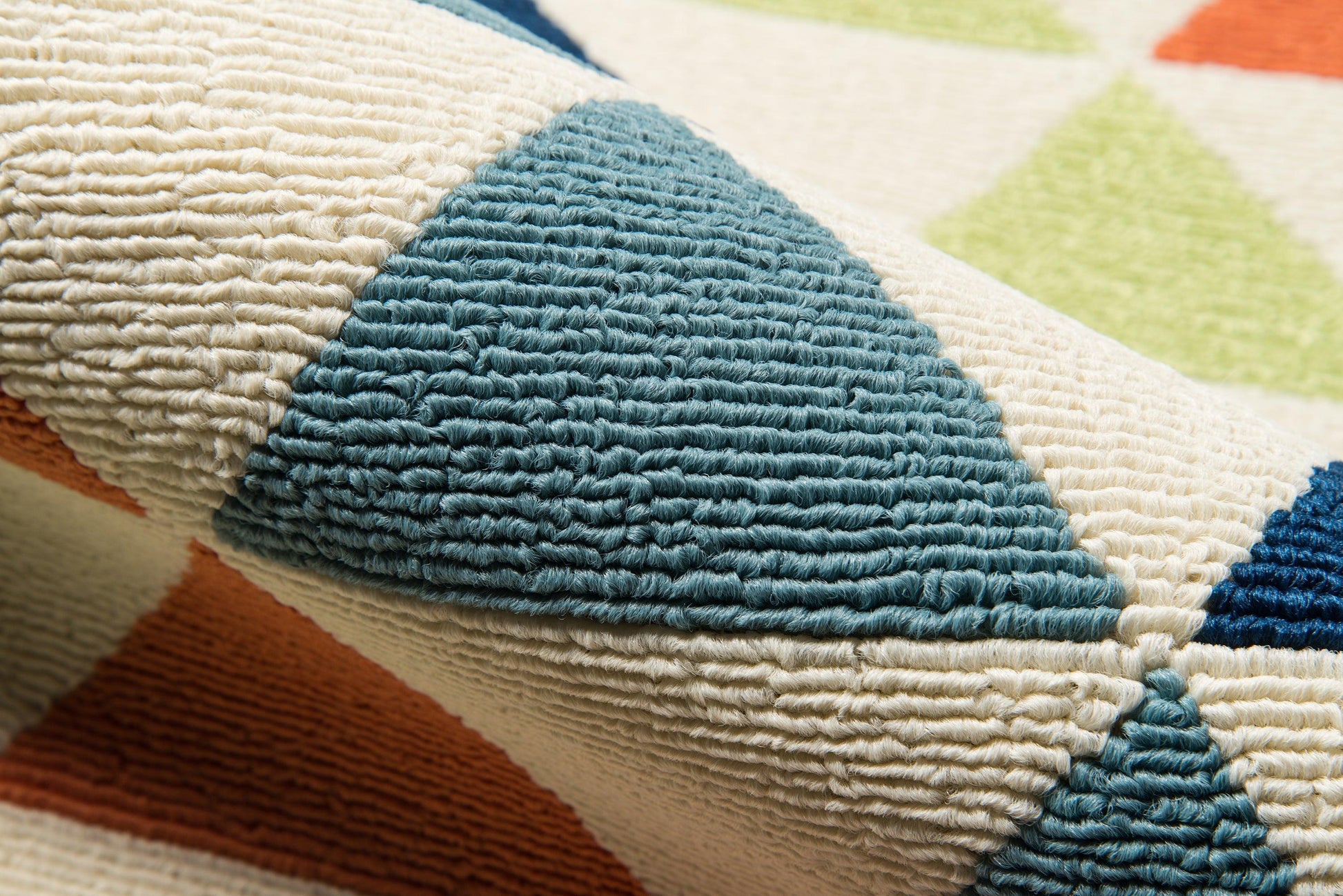 Chunky woven rug close-up with teal blue triangles on cream background and orange and lime accents.