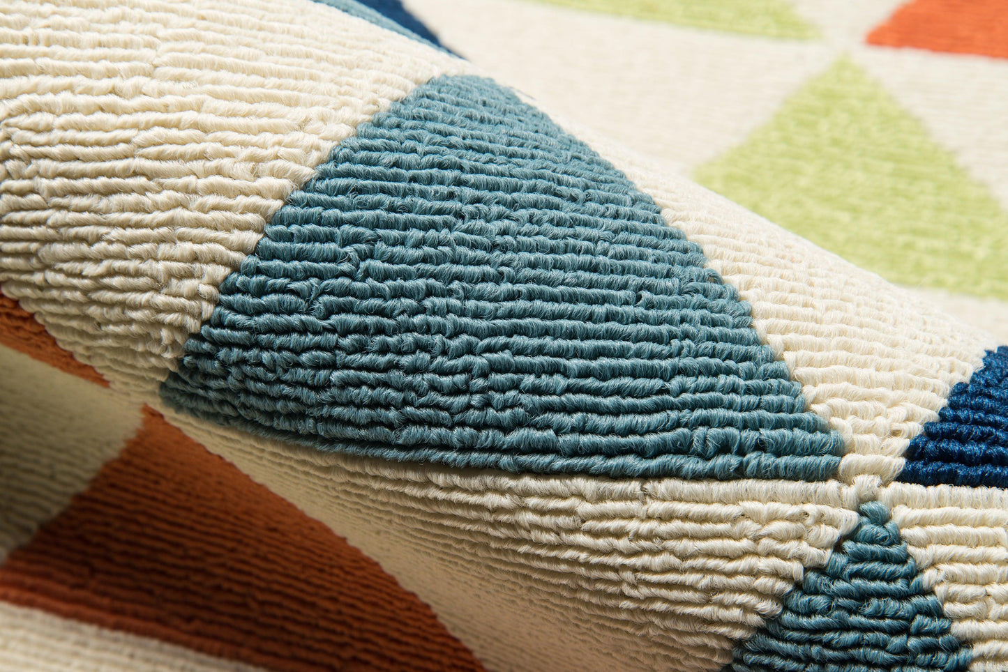 Chunky woven rug close-up with teal triangle motifs on cream background and orange and lime accents, geometric pattern.