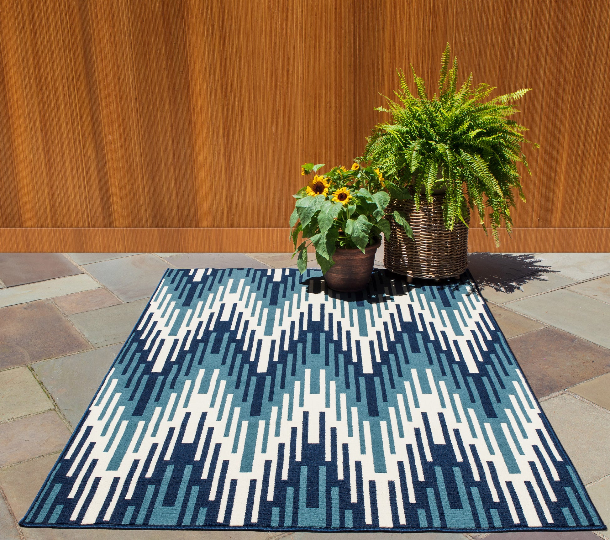 Rectangular outdoor rug in navy, teal and white zigzag pattern with sunflowers in a ceramic pot and a fern in a wicker basket