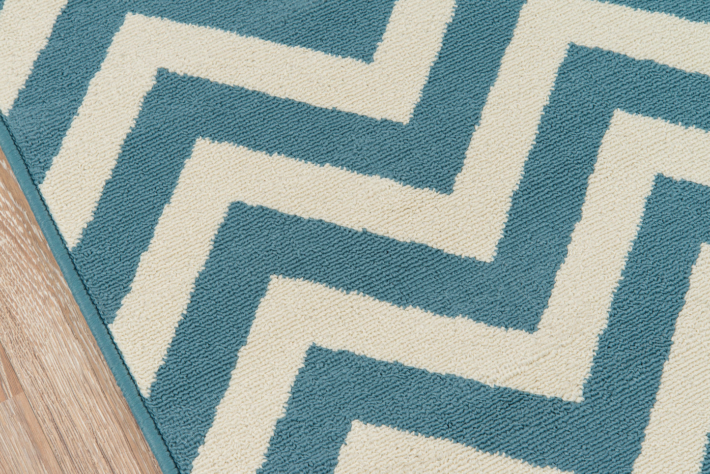 Teal and cream rug with a bold Greek-key zigzag pattern on a wooden floor.