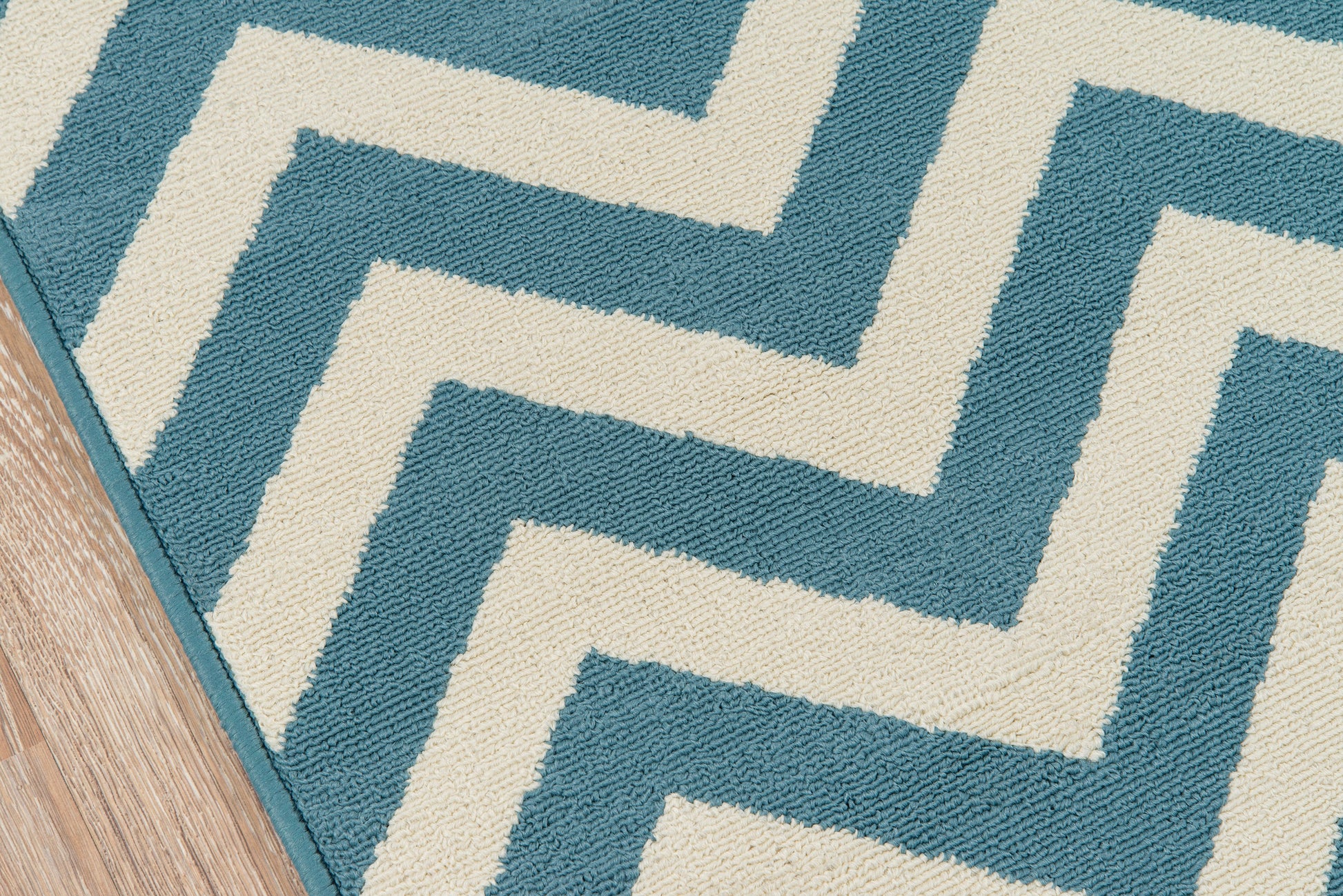 Teal and cream rug with a bold Greek-key zigzag pattern on a wooden floor.