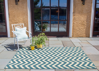 Outdoor patio scene with blue-beige chevron rug, white metal chair with light blue cushion, and potted plants in yellow pots.