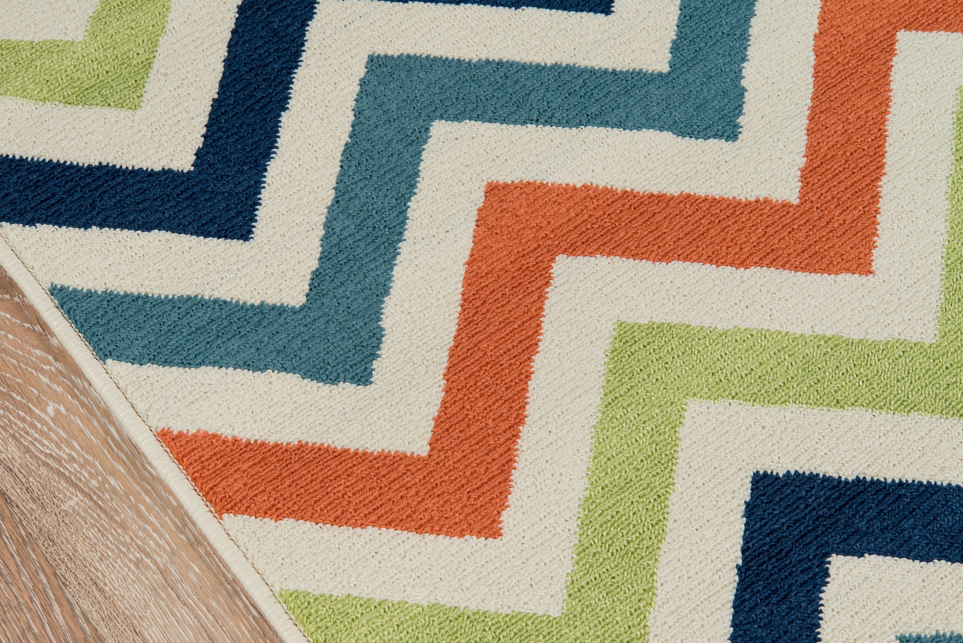 Multicolor geometric zigzag rug with cream base and blue, teal, orange and lime green accents on a wooden floor.