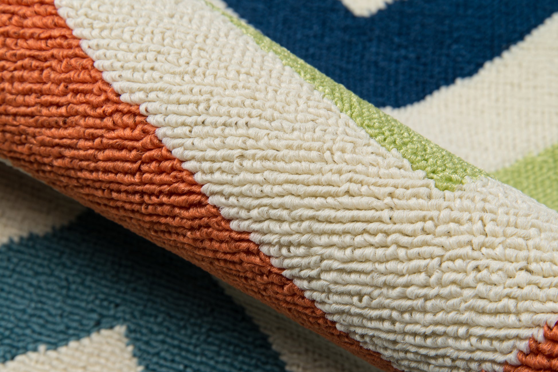 Close-up of a textured striped rug in orange, cream, teal and lime green; looped pile.