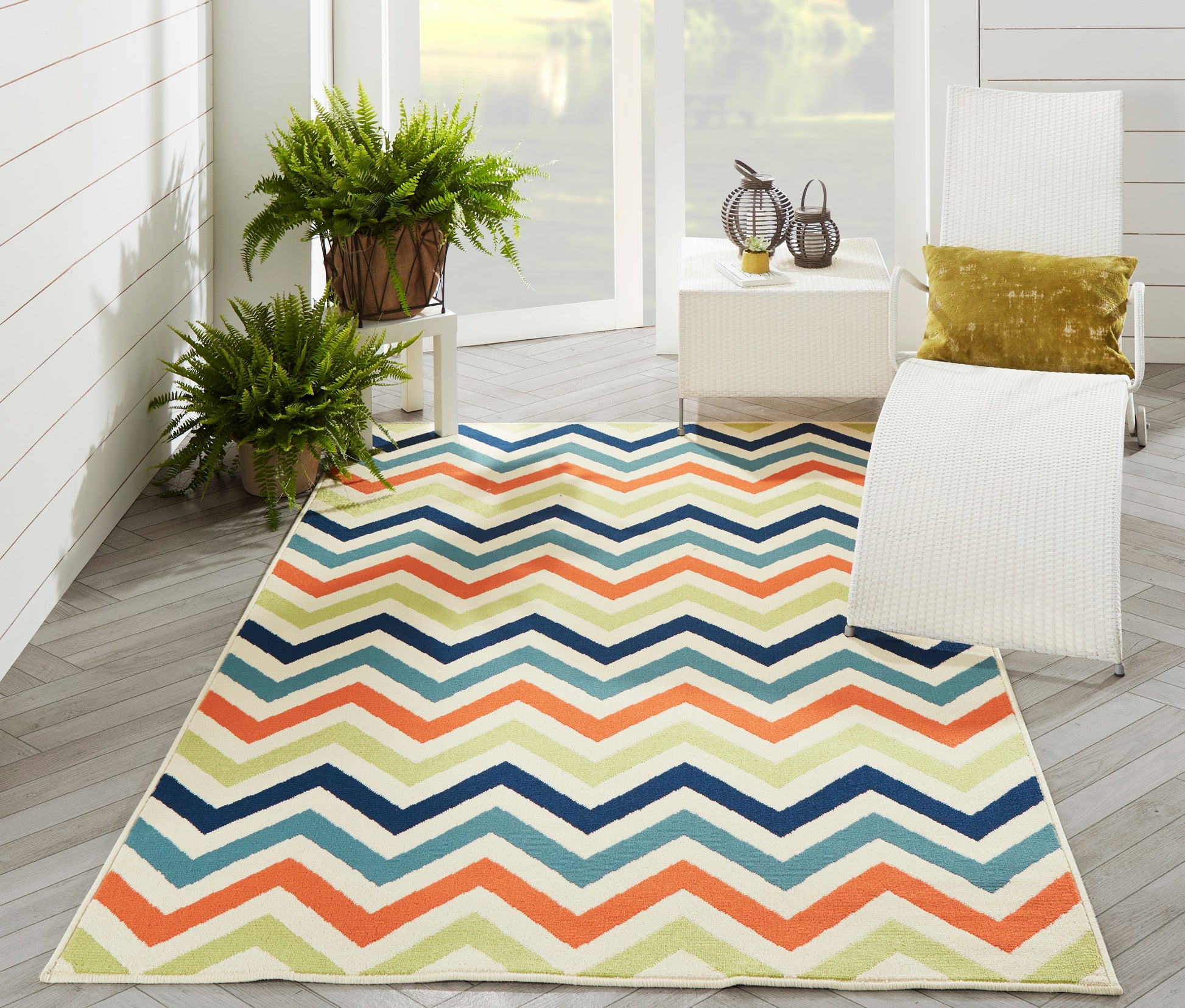 Outdoor chevron rug with navy, teal, orange, lime zigzags on gray deck & white wicker chairs.