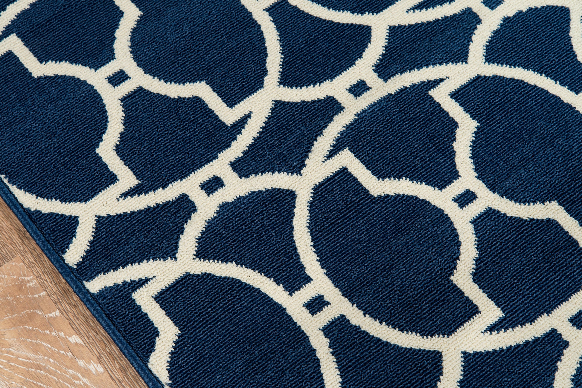 Navy blue rug with cream circular lattice pattern and visible edge binding on wooden floor.