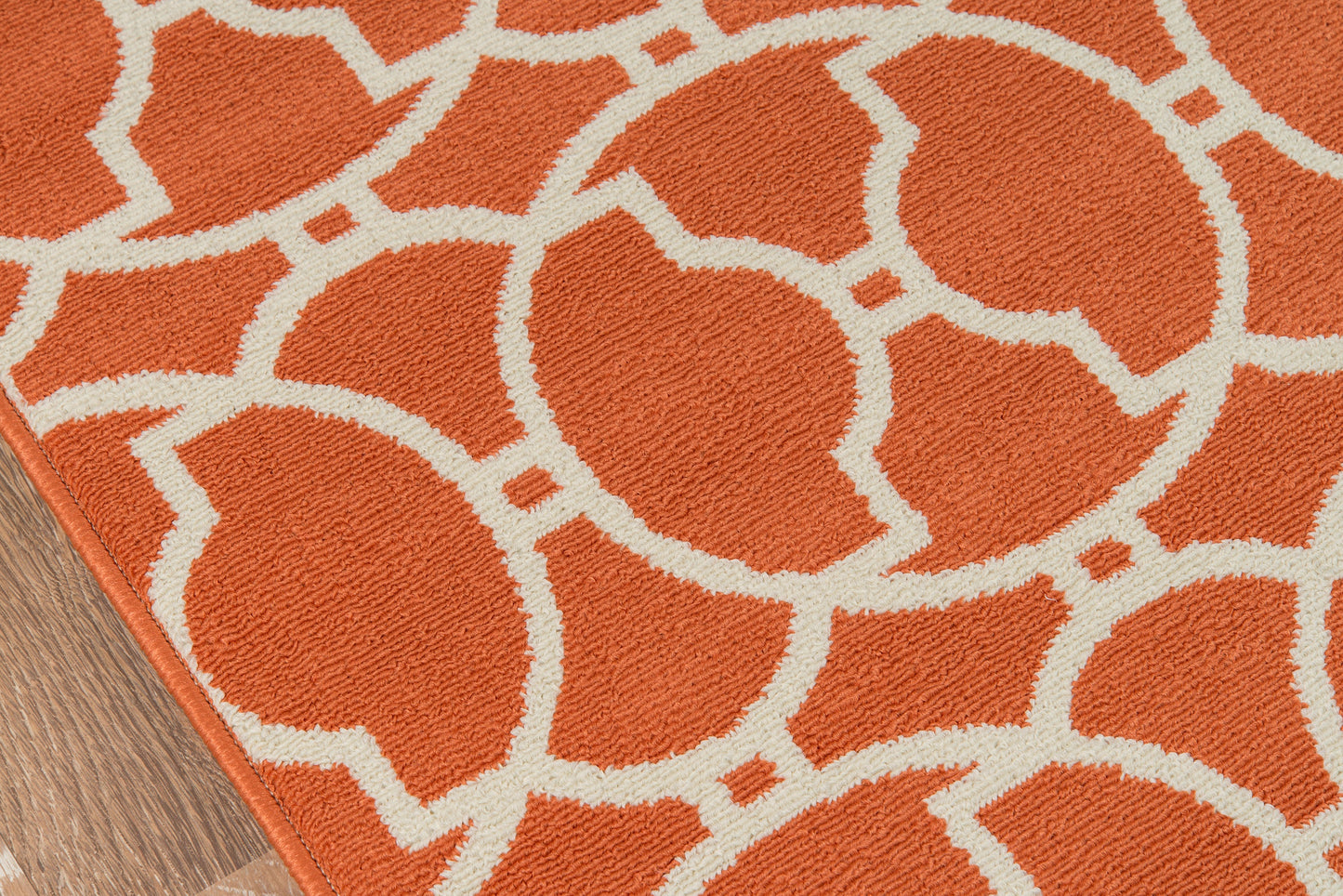 Orange area rug with white interlocking circular lattice pattern on wood floor.