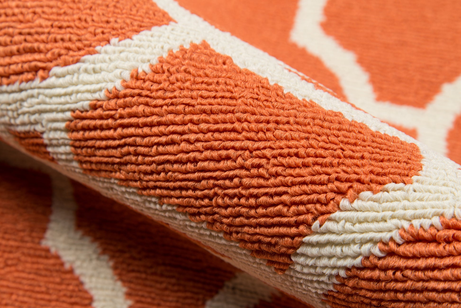 Close-up of an orange and white geometric rug with a raised loop pile and textured weave.