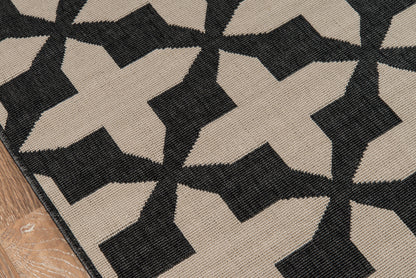 Beige and black woven rug with bold star-like geometric pattern; textured flatweave on wood floor edge.