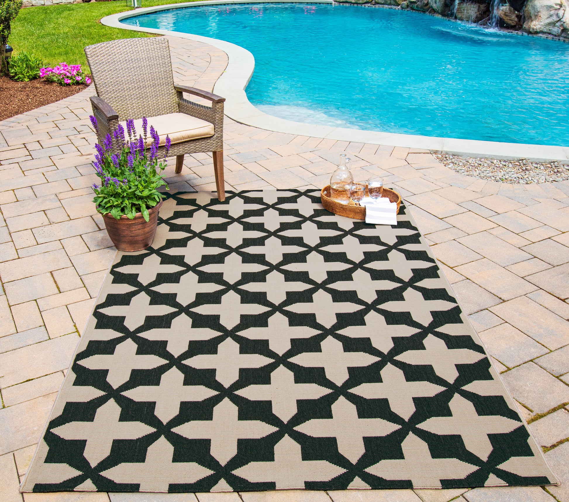 Outdoor poolside rug (2' x 4') with a beige and black geometric pattern, wicker chair, potted lavender, and a drinks tray.