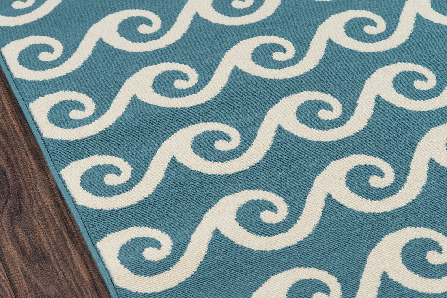 Blue Baja rug with white spiral wave pattern; close-up showing wood floor edge.