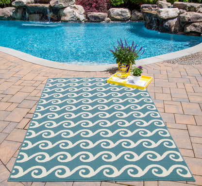 Rectangular teal outdoor rug with white wave pattern on brick pool patio; yellow tray with potted lavender nearby.