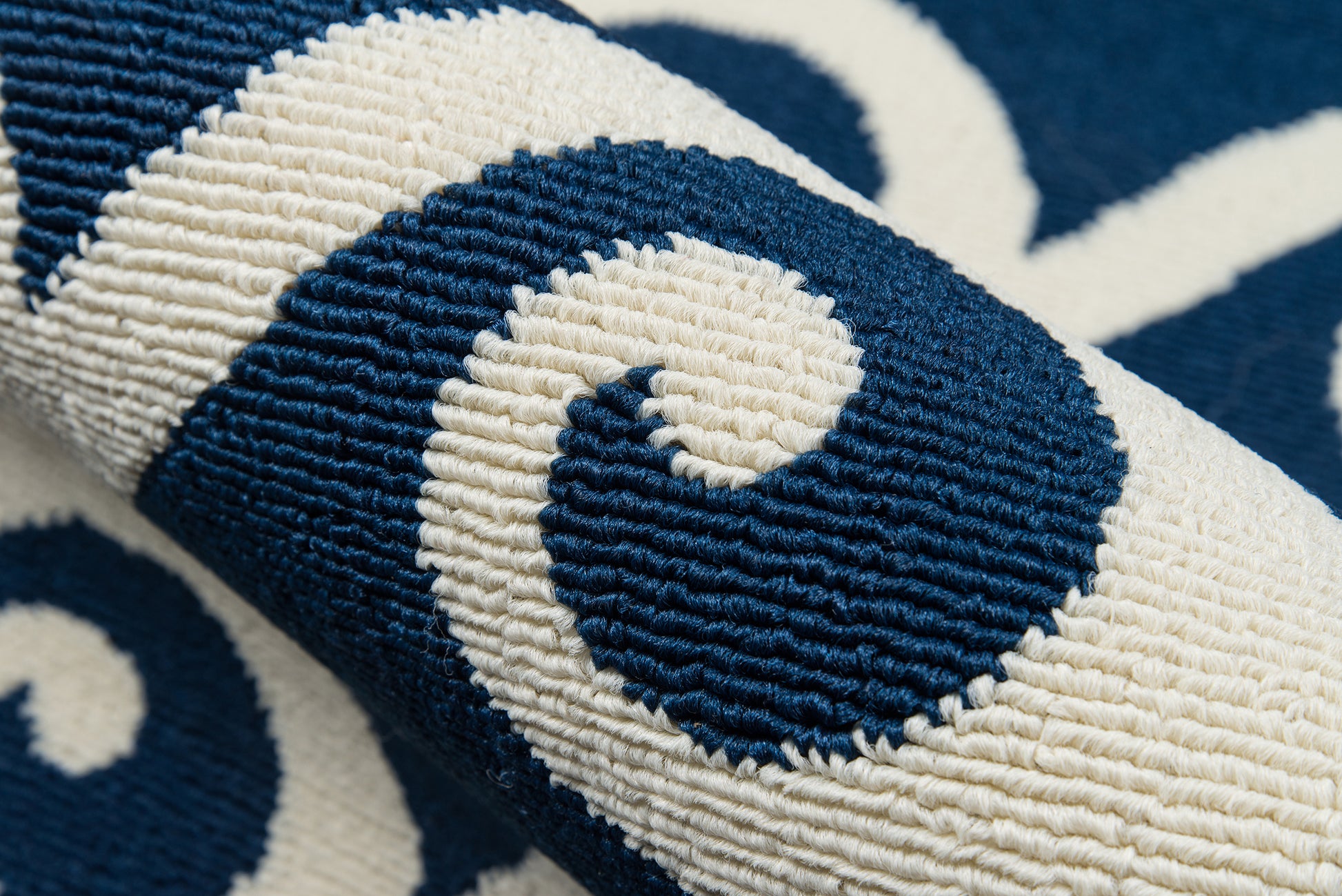 Close-up of navy blue and ivory woven rug with a curving scroll motif and thick tufted pile.