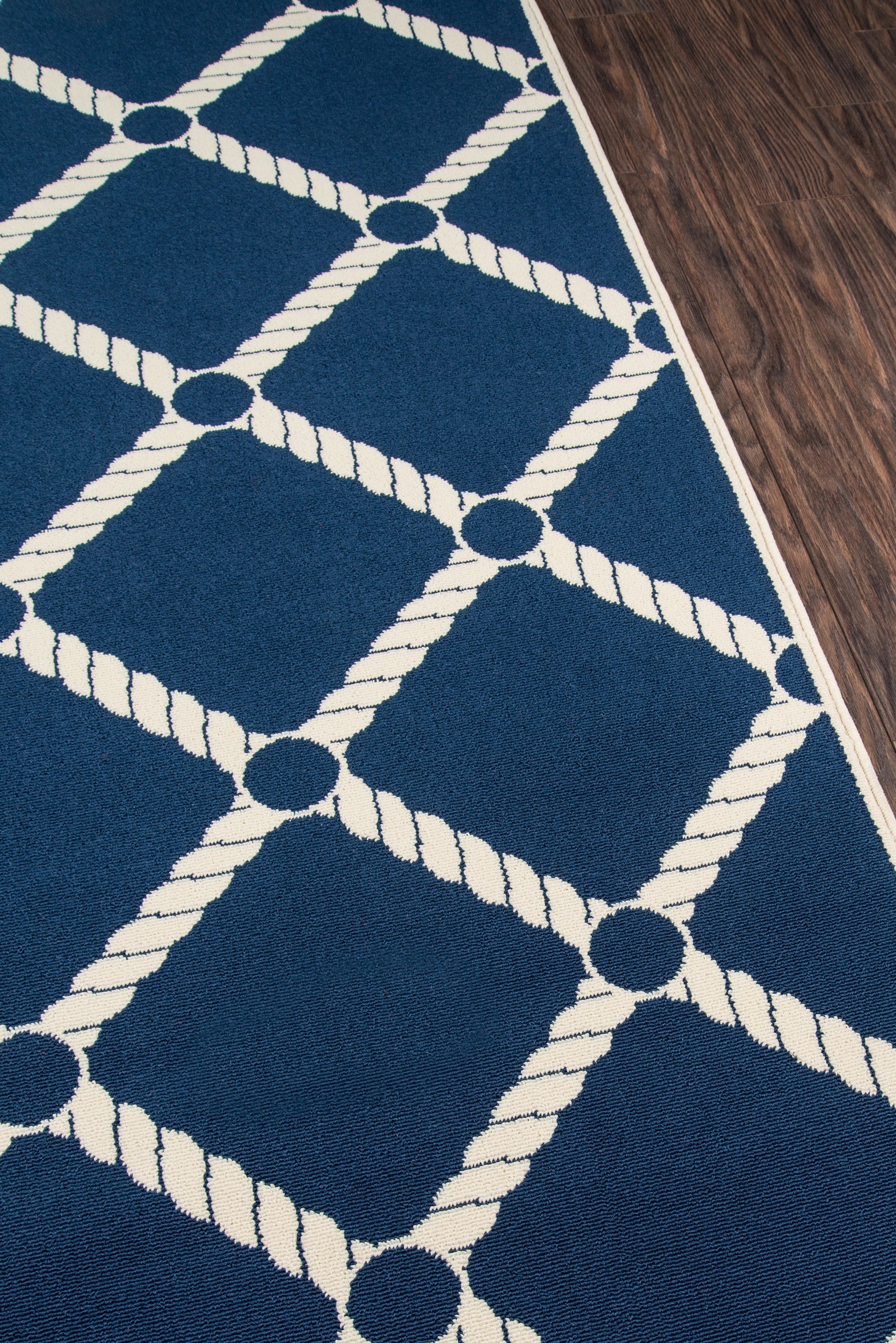 Blue rug with white rope lattice pattern forming diamonds on a wood floor; nautical geometric style.